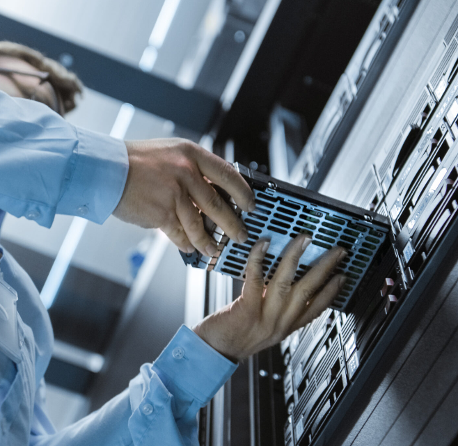 Mains d'un technicien informatique insérant un composant matériel dans un rack de serveurs.
